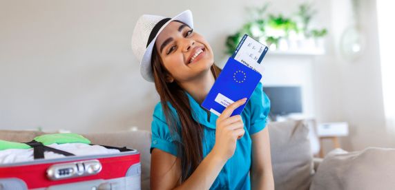 Joven estudiante sonriente mostrando su pasaporte europeo y boleto de avión lista para viajar