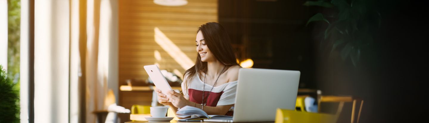Joven usando una tablet en una cafetería con laptop y libros abiertos